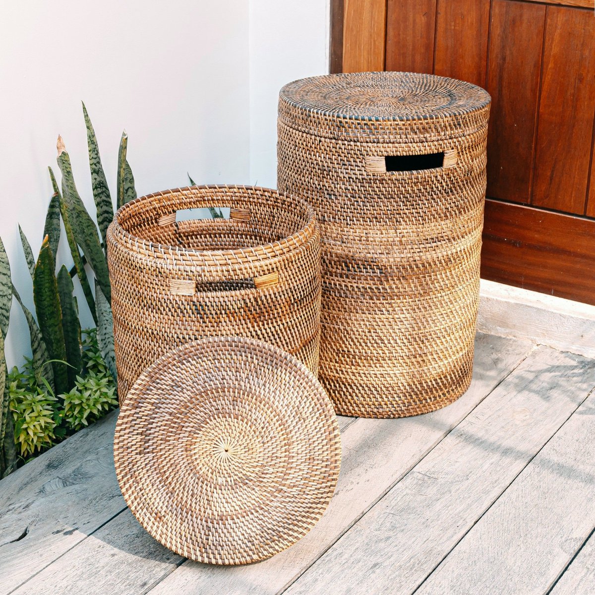 Twee rotan wasmanden met deksel naturel Sari op een houten vloer, van de kleine mand ligt de deksel op de grond