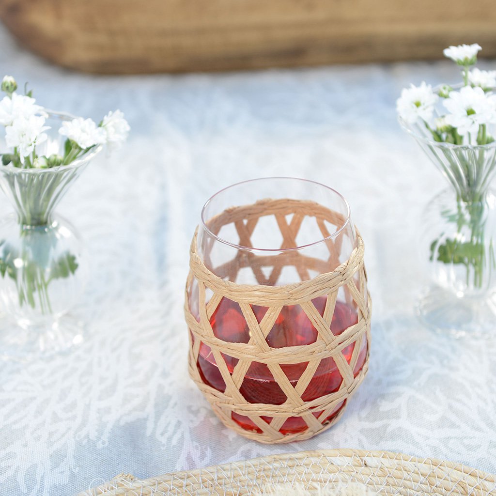 Waterglas met rotanomhulsel met ranja erin, op een gedekte tafel met witte bloemetjes