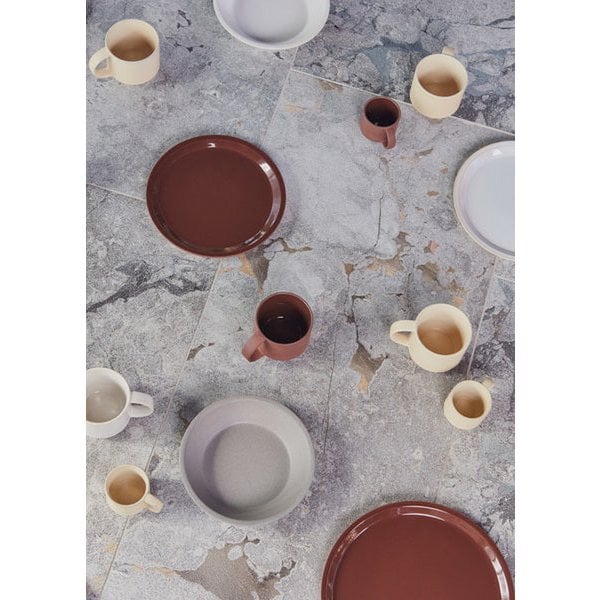 Keramieken mokken en borden in aardetinten op natuurstenen ondergrond – modern servies in beige, bruin en grijs.