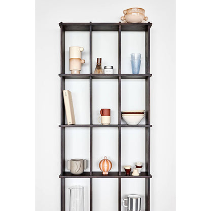 Designservies in aardetinten op zwarte houten kast – keramieken mokken, kommen en glazen als moderne woondecoratie.