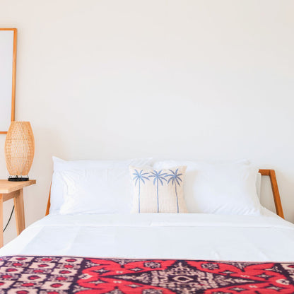 Witte kussenhoes met blauw palmmotief Anarka gestyled op een beachy style bed