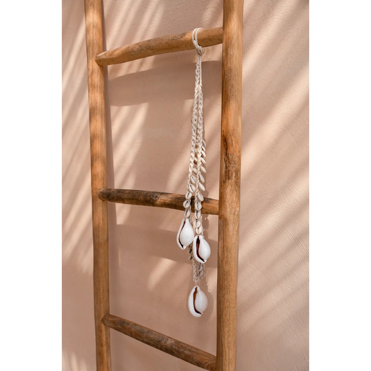 Bohemian schelpketting met witte cowrie schelpen aan wand