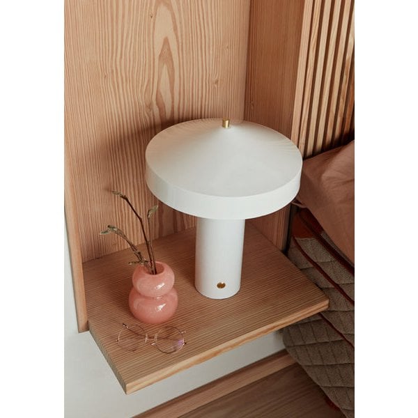 Witte tafellamp geplaatst in een houten slaapkamerhoek met zachte decoratie.