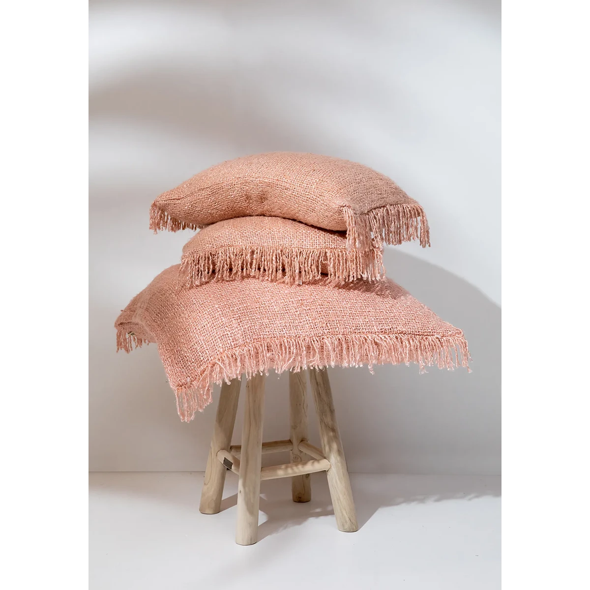 Stapel zalmroze kussens op houten krukje