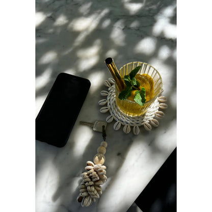 Zeegras onderzetter wit met schelpen 23 cm op een tafel samen met een schelpen sleutelhanger en een smoothie