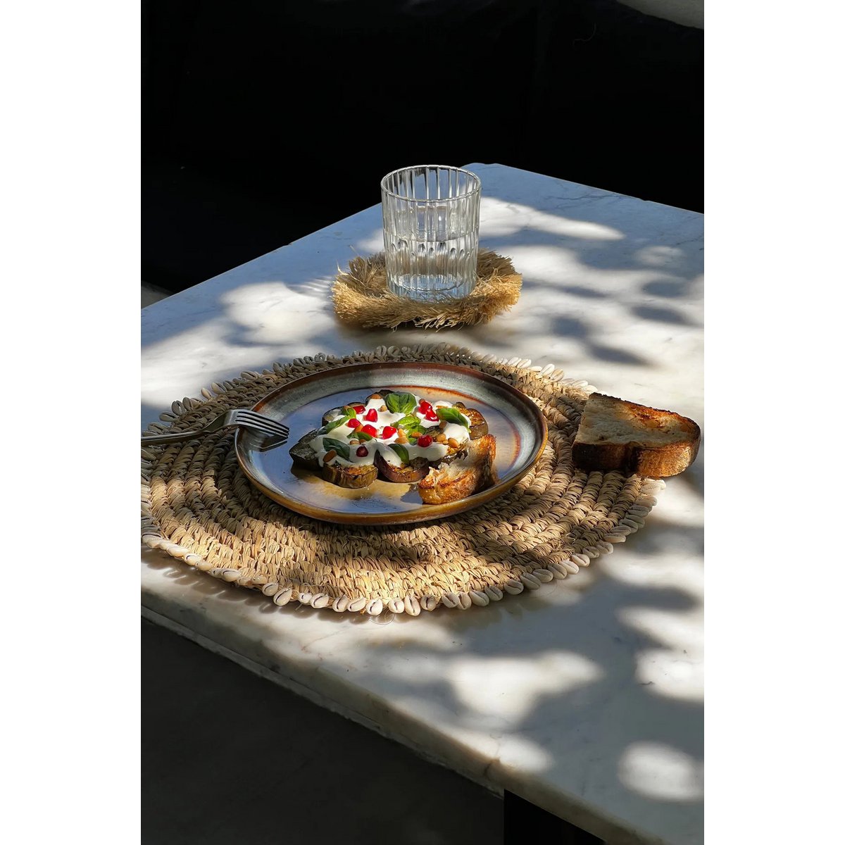 Zeegras placemat met schelpen naturel 38 cm buiten om tafel met daarop een bord met lekker eten