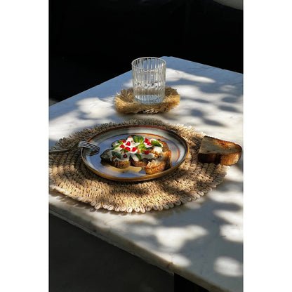 Zeegras placemat met schelpen naturel 38 cm buiten om tafel met daarop een bord met lekker eten