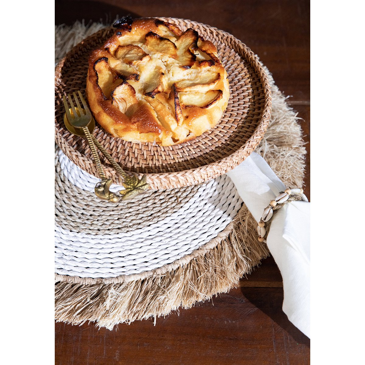 Zeegras raffia placemat naturel wit 45 cm met daarop een gevlochten schaal met een taart erop en een servet ernaast
