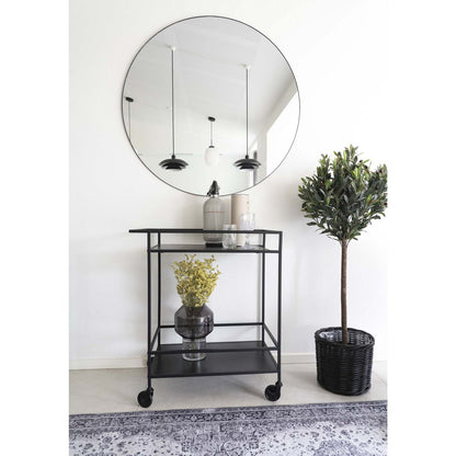Zwarte bar cart gestyled in interieur naast spiegel en plant, serveerwagen op wielen in hal