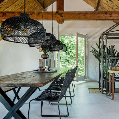 Meerdere zwarte rotan Jane stoelen aan een lange houten eettafel, met zwarte rotan hanglampen erboven in een lichte ruimte met houten dakbalken.