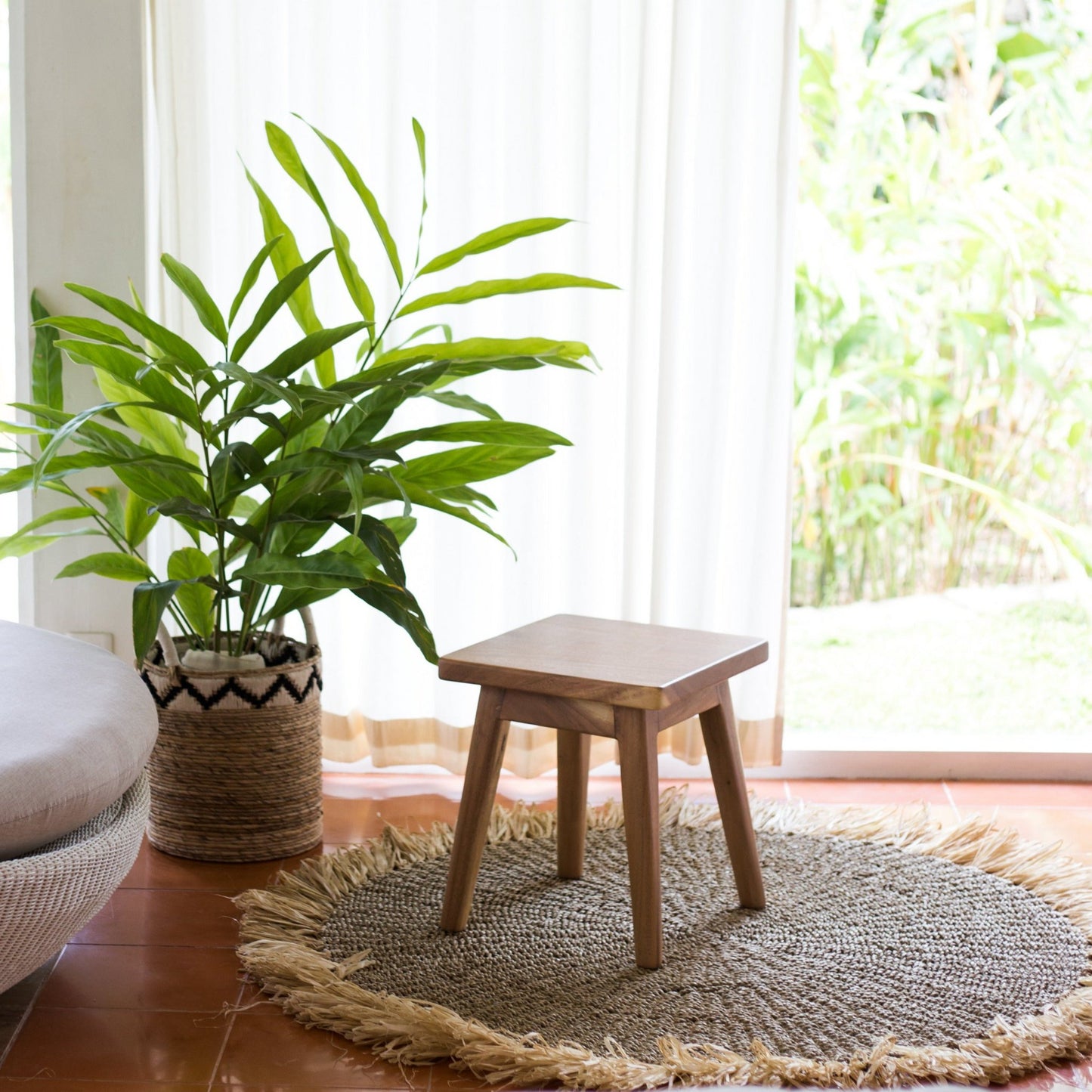 Rond vloerkleed van zeegras Dasa gestyled in een woonkamer met plant en kruk op de achtergrond