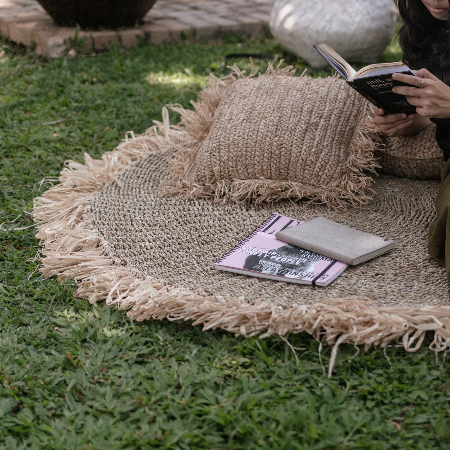 Rond vloerkleed van zeegras Dasa buiten op het gras, aangekleed met boeken en kussentjes