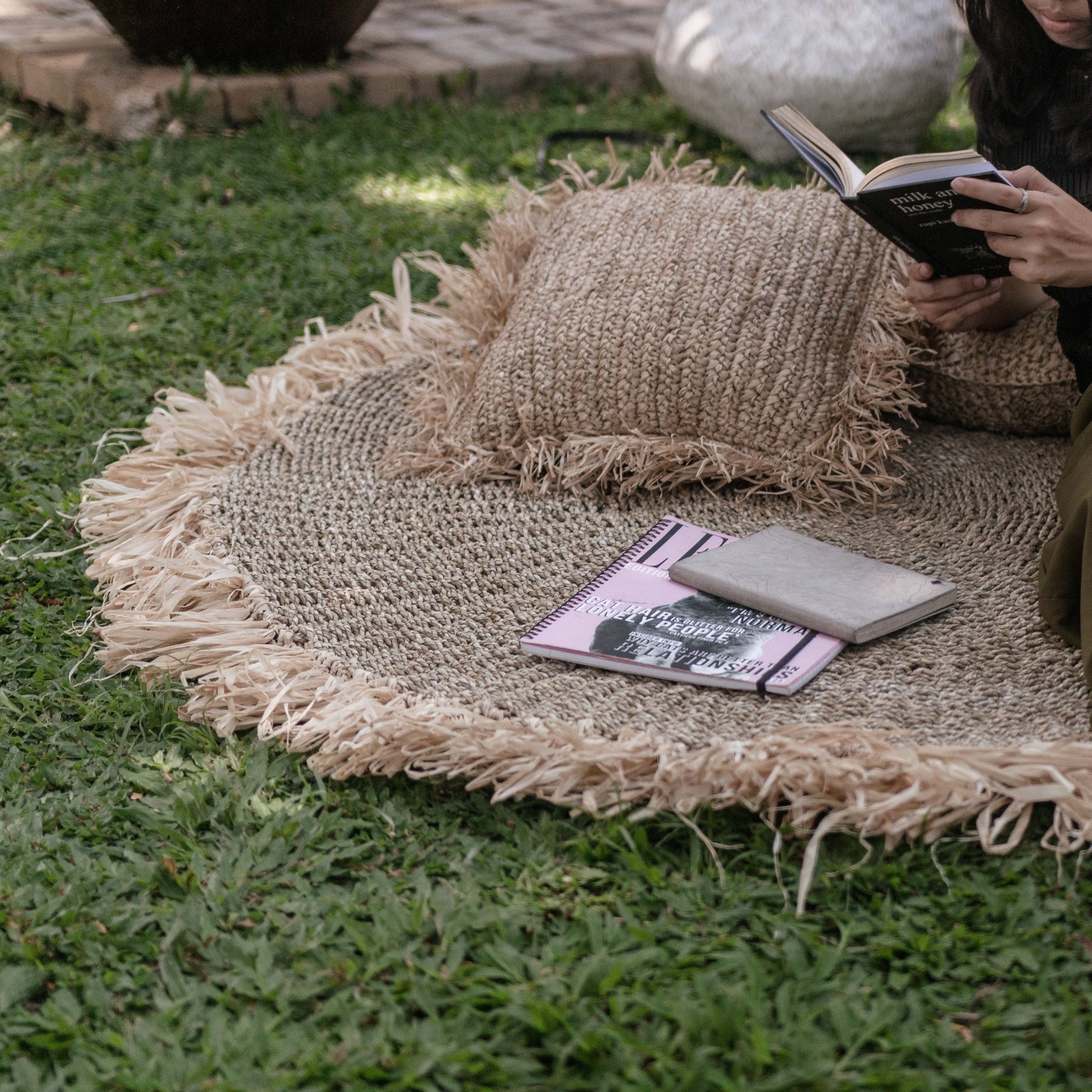Rond vloerkleed van zeegras Dasa buiten op het gras, aangekleed met boeken en kussentjes