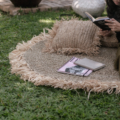 Rond vloerkleed van zeegras Dasa buiten op het gras, aangekleed met boeken en kussentjes