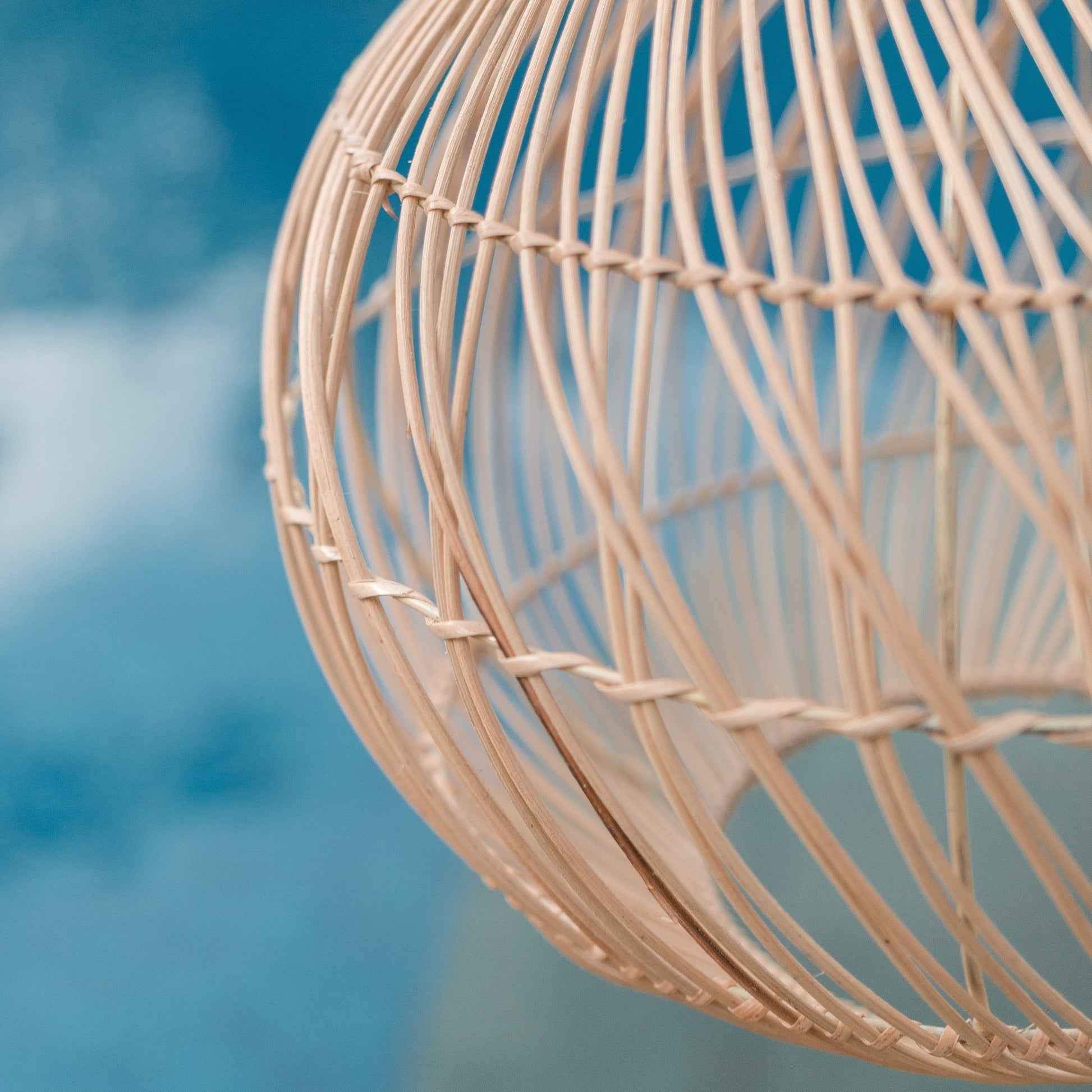 Closeup detail foto van de Rotan hanglamp Kenari, met op de achtergrond water. Perfect voor een boho of Ibiza lifestyle.