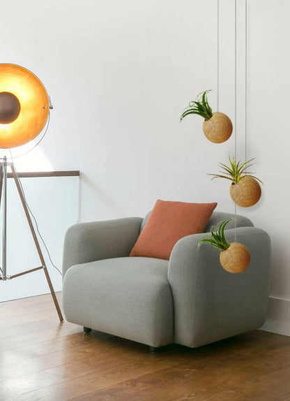 Drie hangende ronde lichte plantenbakken naast een grijze fauteuil met rood kussen