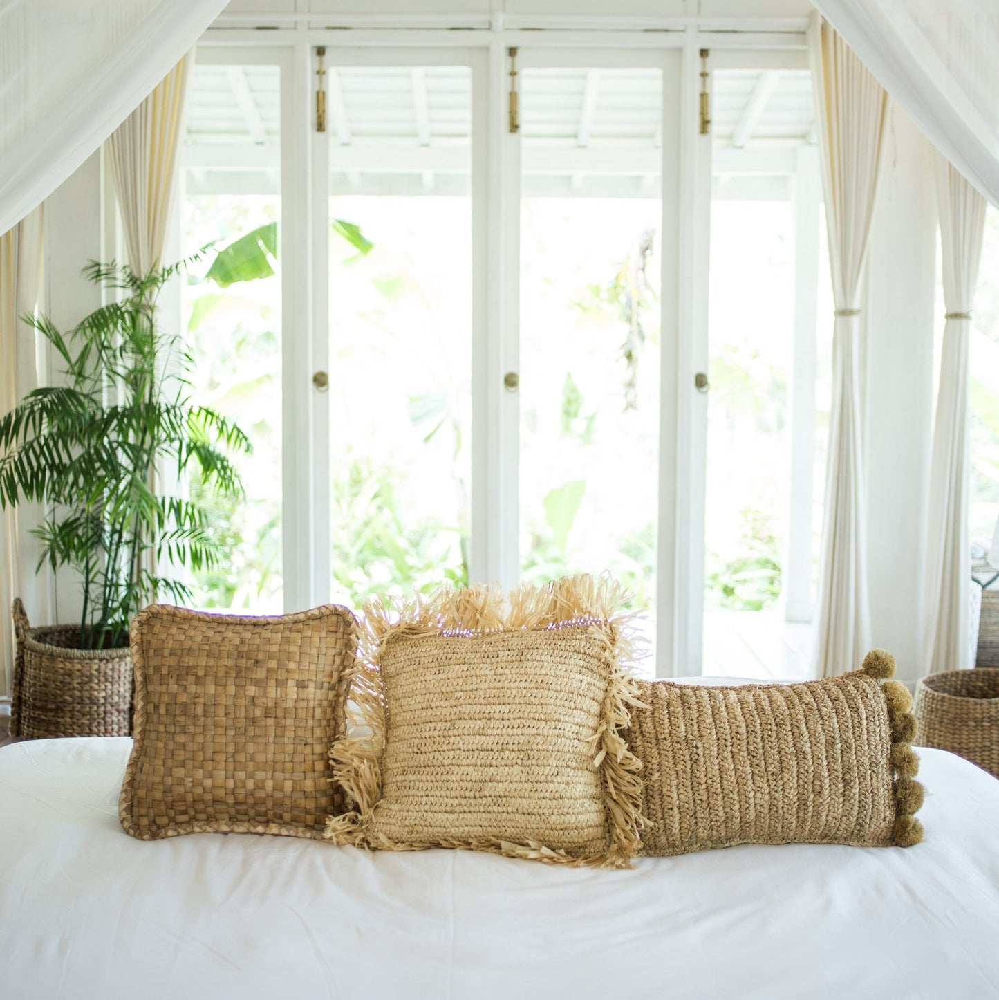 3 Raffia sierkussens naast elkaar op een bed in een slaapkamer