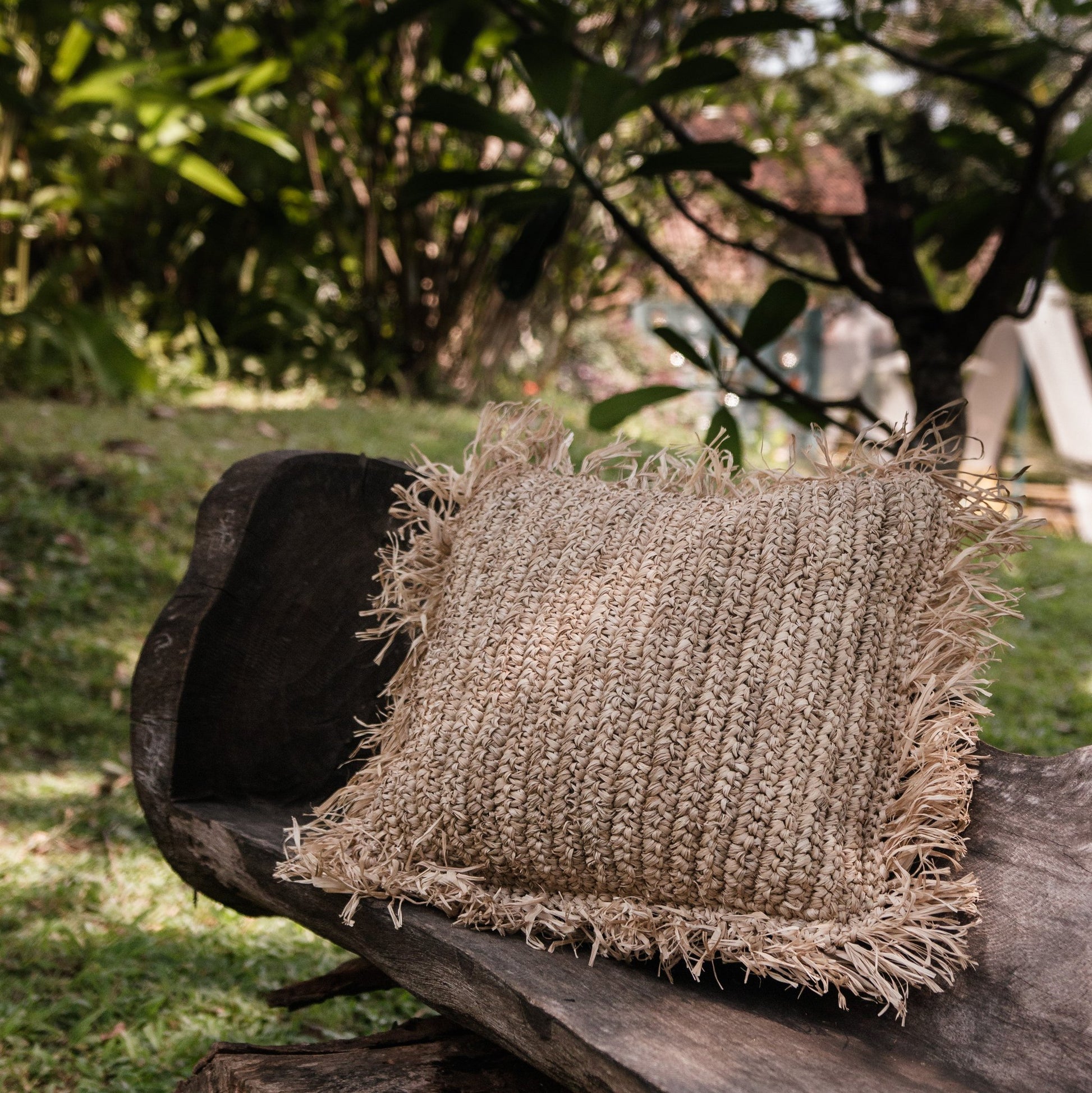 Sierkussen raffia met franjes Gandi op een bankje buiten in de natuur